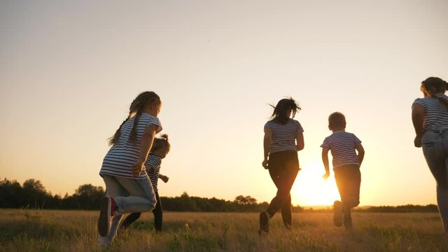 Happy family, mom, dad, son and daughters run across the field in the Park. Happy family at sunset in the rays of the sun running through a green field. teamwork. The concept of a happy family.