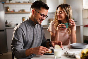 Beautiful woman enjoying in breakfast with her boyfriend. Happy young couple drinking coffee and eating sandwich at home.