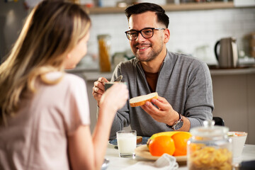 Beautiful woman enjoying in breakfast with her boyfriend. Happy young couple drinking coffee and eating sandwich at home.