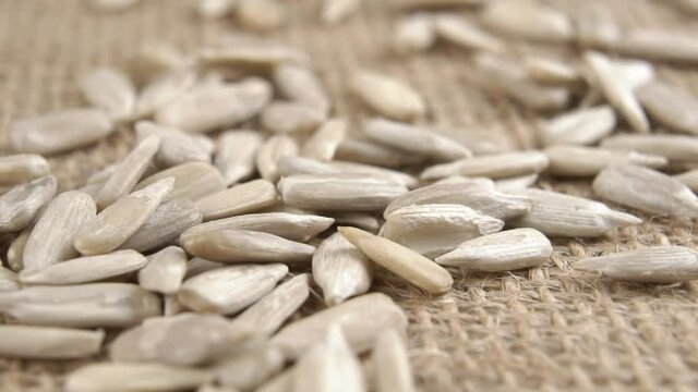 Detailed peeled raw sunflower seeds fall onto a textured burlap mat in slow motion. Macro