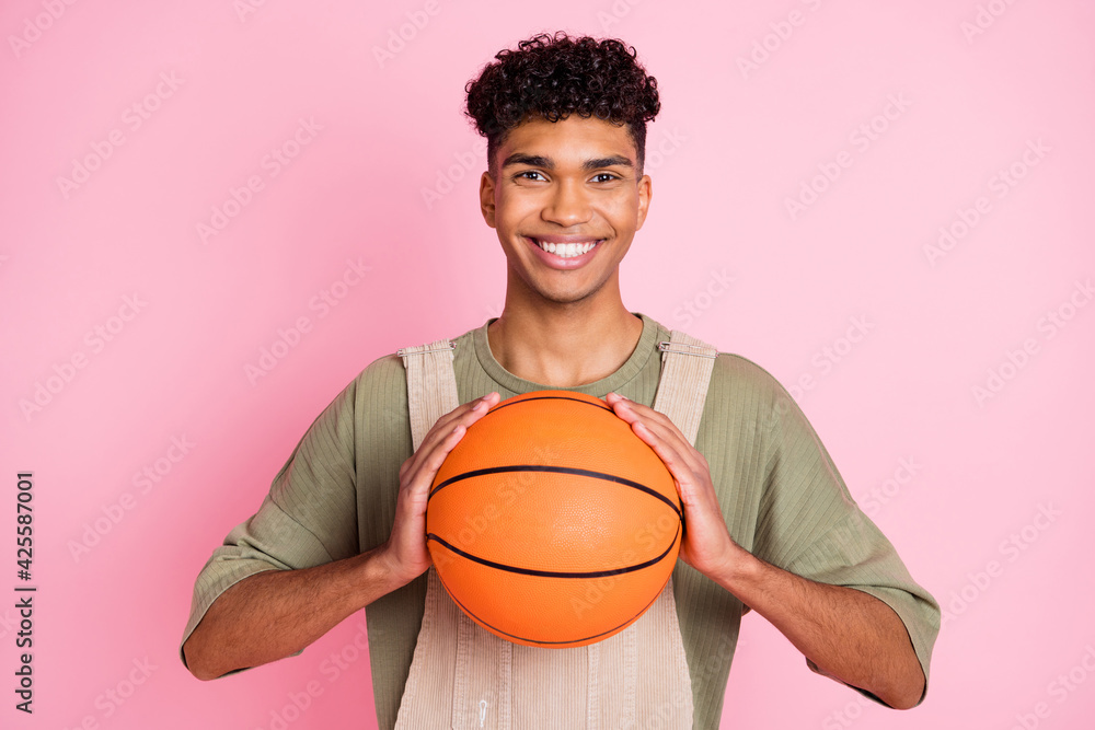 Sticker Photo portrait of curly guy keeping ball on training smiling in stylish clothes isolated on pastel pink color background