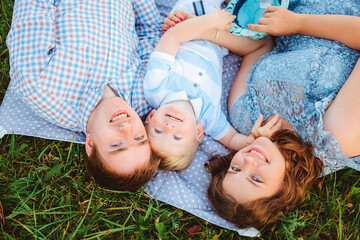 A family with a son in nature. Mom, dad and baby are lying on the grass and looking up.