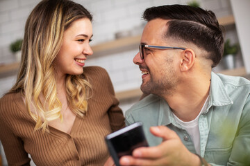 Loving couple in the kitchen. Happy smiling boyfriend and girlfriend using the phone, reading the news online