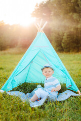 Child and wigwam for kids. The little boy sits on the grass and rests in nature.