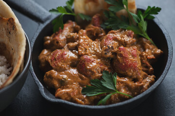 Cast-iron skillet with indian butter chicken masala, closeup on a black stone background, selective focus