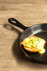Delicious eggs benedict presented in a frying pan on a wooden table ready to eat. Healthy breakfast