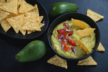 Bowl of guacamole dip sauce with corn chips, studio shot over black stone background, selective...