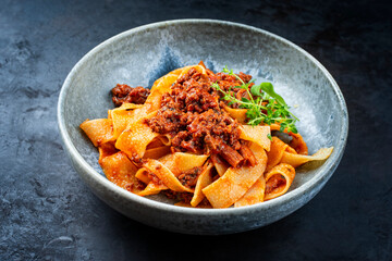 Modern style traditional Italian ragu alla bolognese sauce with papedelle pasta noodles and parmesan cheese served as close-up in a ceramic design bowl with copy space
