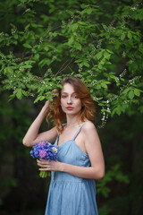 beautiful girl in a denim sundress walks with a bouquet of hyacinths in the garden, spring mood