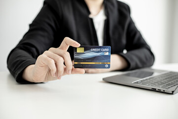 A business woman holds a credit card to make payments on the website where she is shopping online. Concept of using credit cards to pay for goods and services on online websites.