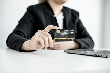 A business woman holds a credit card to make payments on the website where she is shopping online. Concept of using credit cards to pay for goods and services on online websites.