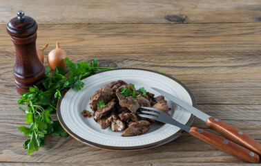 Cooked chicken liver with onion on a plate served on wooden desk. Rustic style