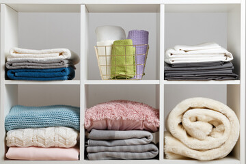 Stacks of towels, sheets, bedding, clothes, blanket and pillow on a white shelf.
