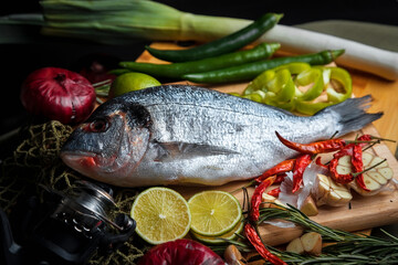 Fresh uncooked dorado or sea bream fish with lemon slices, spices, herbs and vegetables. Mediterranean cuisine. 