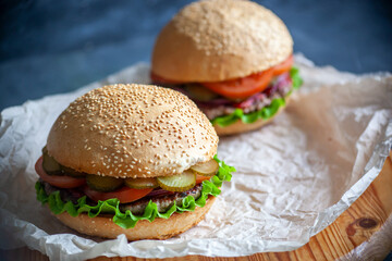 Two hamburgers lie on the board on a dark background