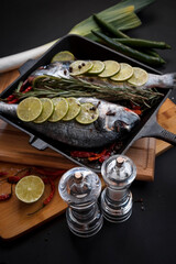 Dorado fish is cooked in a black grill pan. Seafood and vegetables. Seasonings and spices.