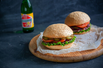 Two hamburgers lie on the board on a dark background