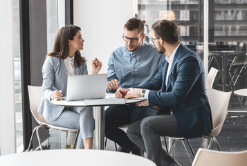 A group of office workers discuss a new company project. They sit at the desk in the company cafe...