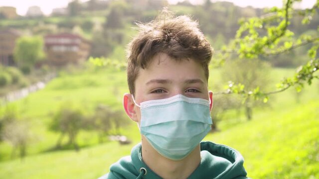 A teenager in a medical protective mask shows a NO gesture with his head against the backdrop of a bright beautiful nature. Surprise and denial concept