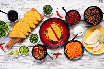 Taco bar table scene with a variety of ingredients. Above view on a rustic white wood background....