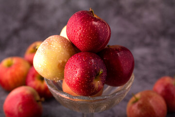 Fresh red and green apples in a glass bowl with water drops.