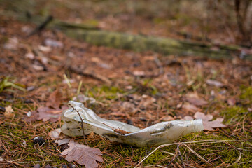 A flattened plastic bottle lies discarded in the forest and does not decompose