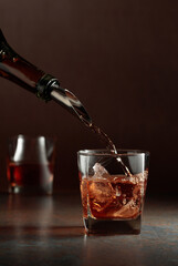 Whiskey is poured from a bottle into a frozen glass with natural ice.