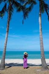 A woman standing with her back on the beach with a coconut tree at Samila beach, Songkhla, Thailand