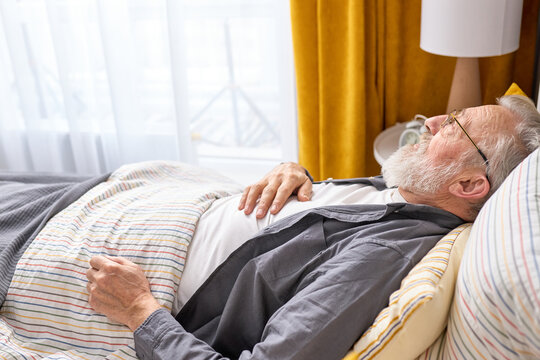 Senior gray bearded man ill, feel bad lying on bed at home alone