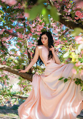 Spring sexy fantasy woman sits on branch green tree blooming sakura flowers garden. Medieval girl...