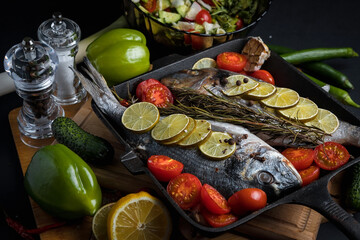 Dorado fish is cooked in a black grill pan. Seafood and vegetables. Seasonings and spices.