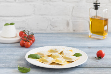Raw ravioli on white plate, with basil leaves, light background
