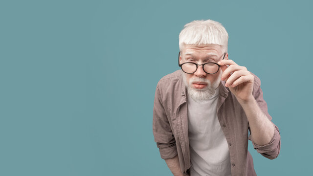 Vision problems. Young albino guy in eyeglasses squinting eyes, blue background, panorama with free space