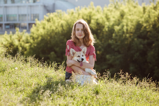 Cute teenager girl hugs welsh corgi pembroke dog outdoors in the city park in summer.