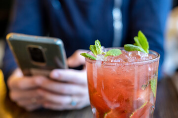 Mojito cocktail and woman with phone in cafe. Rest, chatting on the phone, paying online concept.