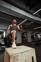 Sexy muscular men using the platform for his legs on a dark colorful background of gym.