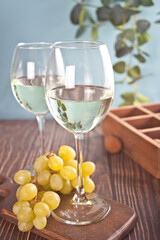 Glasses of white grape wine with grapes and wooden box on the background