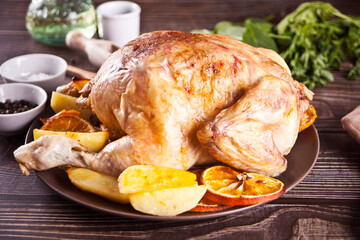 Roasted whole chicken with oranges and potatoes on a plate.