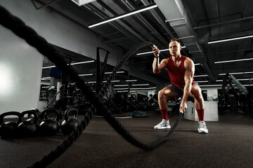 Fototapeta na wymiar Sport. Strong man exercising with battle ropes at the gym with. Athlete doing battle rope workout at gym. Dramatic sports background.