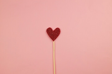 Decorative shiny red heart on a stick on a pink background.