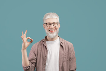 Everything is okay. Joyful albino guy doing approval ok gesture with fingers, showing that he is fine, blue studio background - obrazy, fototapety, plakaty