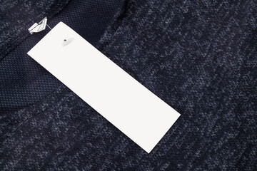 White rectangular clothing tag, blank label on dark blue dress. Close up of empty price tag on cloth.