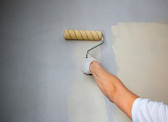 mans hand in cloth glove with paint roller applies fresh paint and primer to wall surface. process...