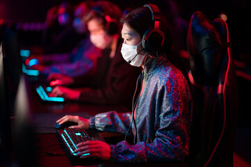 Fototapeta na wymiar The dota 2 tournament in the conditions of covid-19 is held in medical masks, gamers play at computers, the team leader is a chinese girl