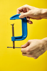 blue c-clamp or G-clamp in male hands, isolated on yellow background