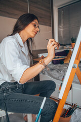 Beautiful talented female artist painting at her home.