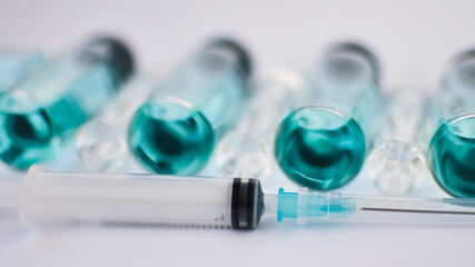 Vial vaccine, top view of glass ampoules with transparent and blue liquid, a syringe is lying near on white background, global vaccination concept