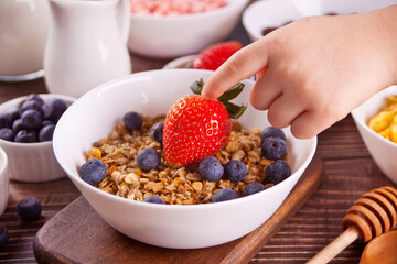 Healthy breakfast. Granola, muesli with fresh berries. Child hand touch a strawberry.
