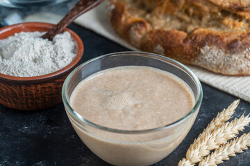 Yeast-free sourdough bread, flour, water and glass jar with dough leaven on the table. Preparing yeast dough for bread