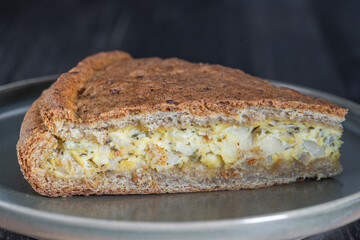 Slice of homemade onion quiche a baked cream and egg pie topped with cheese and green herbs